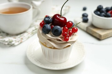 Tasty cupcake with different berries and tea on white marble table, closeup