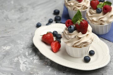 Tasty cupcakes with different berries and mint on light grey table, closeup. Space for text