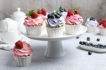 Tasty cupcakes with different berries on light grey table