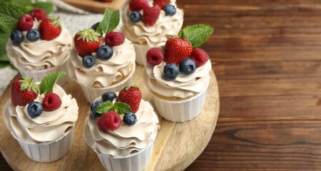 Tasty cupcakes with different berries and mint on wooden table, closeup. Space for text
