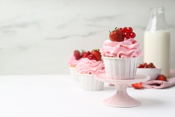 Tasty cupcakes with strawberries and red currants on white table, space for text