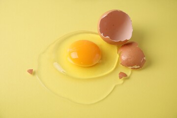 Broken raw egg and shell on yellow background, closeup