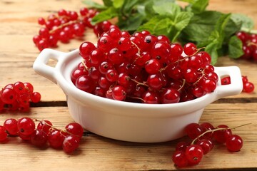 Fresh red currants in bowl and mint on wooden table, closeup