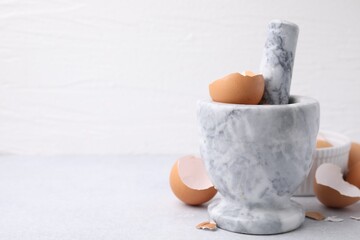 Broken eggshells, mortar and pestle on grey table, closeup. Space for text