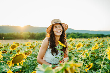 One beautiful young caucasian woman is in sunflower field checking on plants and sunflowers during the day