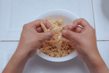Hands of a chef preparing boiled chicken, shredding chicken
