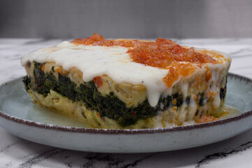 Pasta. Closeup up view of a piece of fish lasagna with cream and tomato sauce on the white marble table.	