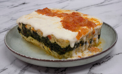 Pasta. Closeup up view of a piece of fish lasagna with cream and tomato sauce on the white marble table. 
