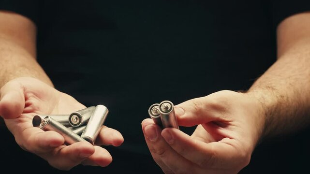 Silver batteries AA and AAA in hands on black background close-up. Double-A battery is a standard size single cell cylindrical dry battery. Batteries are common in portable electronic devices. An AA