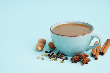 Cup of tasty masala tea with different spices on blue background