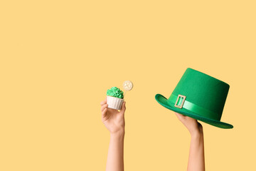 Female hands with tasty cupcake and leprechaun hat for St. Patrick's Day on beige background