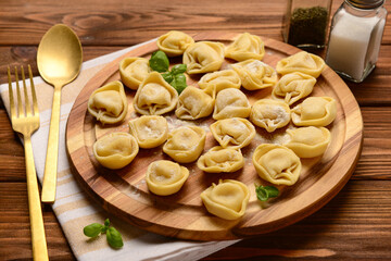 Board with raw dumplings and basil on wooden background