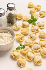 Raw dumplings with basil and bowl of flour on white background