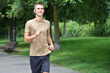 Young man running in urban park, teenager jogging with headphones, in motion