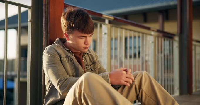 Boy, student and teen thinking on high school with social anxiety, stress and academic pressure or overwhelmed. Male learning, alone and sad on balcony with thoughts of exam, education and burnout.