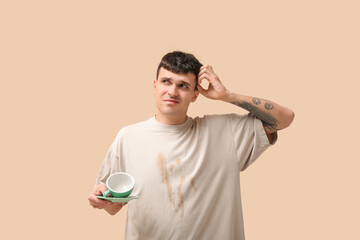 Young man with coffee stains on his t-shirt on beige background