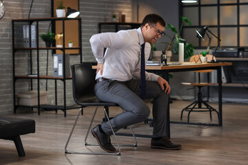 Young businessman suffering from back pain in office at night