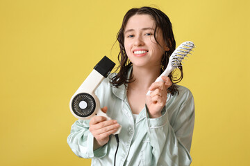 Obraz premium Beautiful young happy woman with brush and hairdryer on yellow background