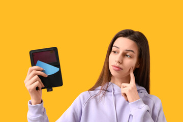 Thoughtful young woman with credit card holder on yellow background