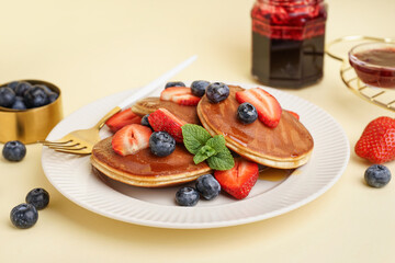 Tasty pancakes with blueberries and strawberry on yellow background