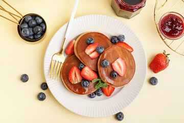 Tasty pancakes with blueberries and strawberry on yellow background