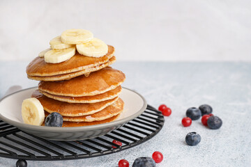 Plate on grate with tasty pancakes and banana slices on white table