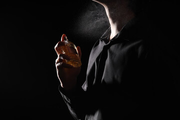 Silhouette of young man with bottle of perfume on black background. Closeup