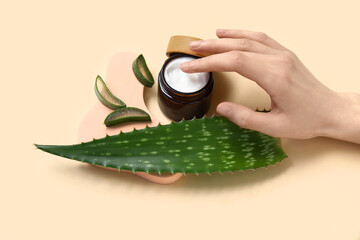Female hand, fresh aloe leaf, jar of cosmetic product and plaster stand on beige background