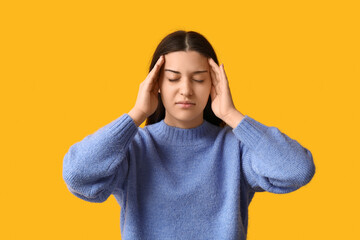 Beautiful young woman suffering from headache on yellow background