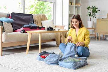 Young woman putting sunglasses into organizer while packing suitcase at home. Travel concept
