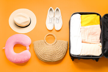 Travel pillow, packed suitcase and beach accessories on orange background