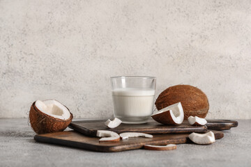 Glass of tasty fresh coconut milk and wooden cutting boards on grunge background
