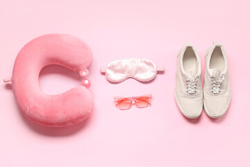 Travel pillow, shoes, sleeping mask and sunglasses on pink background
