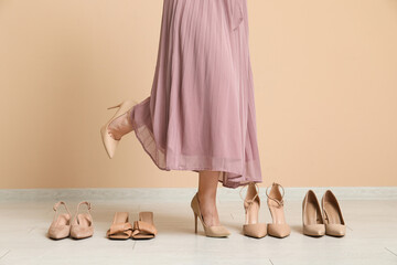Stylish young woman in pink dress with different shoes near beige wall