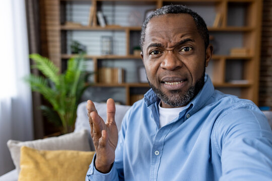 Portrait of man on video call showing frustration or confusion. Casual setting with home decor in background. Concept of remote communication, emotional expression, and technology.