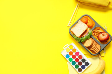 School supplies, lunch box with sandwich and apricot on yellow background. Top view