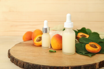 Bottles of cosmetic oil with fresh apricots on wooden background