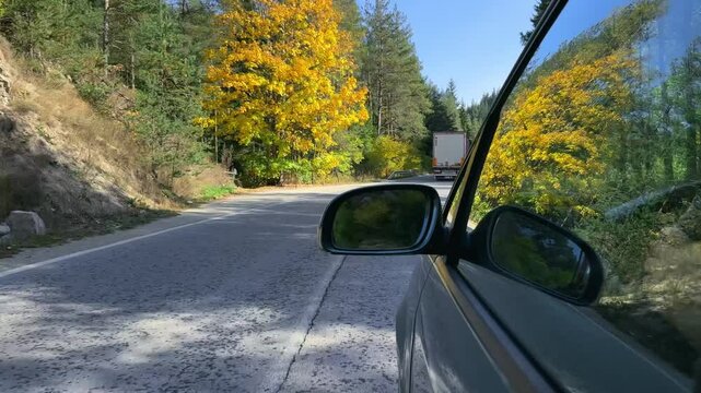 Travel concept. Secret agent drive black luxury car down a mountain road following a trafficking white truck with focus on side mirror . The road is lined with green mountain trees