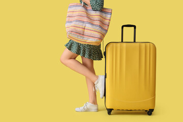 Young woman with suitcase and bag on yellow background