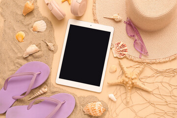 Tablet and beach accessories with flip-flops, starfish and sand on beige background. Top view