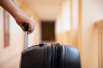 Close-up of hand pulling black suitcase with retractable handle down hallway, evoking sense of...