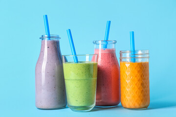 Glasses and bottles of different fresh smoothie on blue background