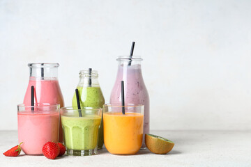 Glasses and bottles of different fresh smoothie with strawberries and kiwi on white background