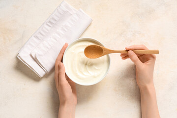 Female hands with bowl of tasty yogurt and wooden spoon on white background