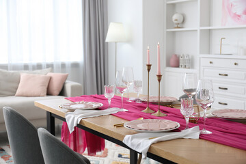 Beautiful table setting with burning candles and pink accent in dining room