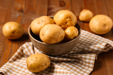 Bowl with raw potatoes on wooden background