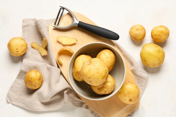 Bowl with raw potatoes and peeler on white background