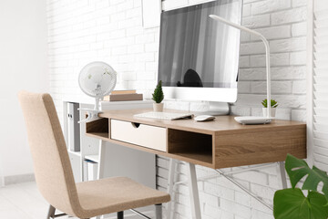 Modern electric fan on table near white brick wall in office