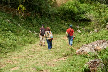 A family group of three unrecognizable adults enjoy the outdoors hiking, walking along a historical and touristic trek between Barichara and Guane, in Santander, Colombia.