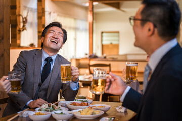 居酒屋で忘年会・新年会・飲み会・宴会で爆笑する中年のビジネスマン男性
